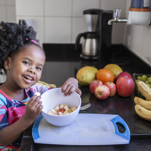 A little girl eating a bowl of fruit.